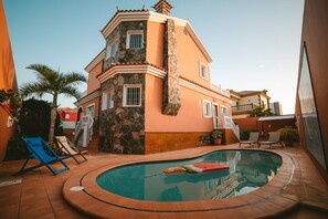 A two-story building with a swimming pool, a stone facade, and a red roof.