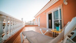 Un balcon doté de balustrades blanches, d’un fauteuil de jardin en osier et d’une petite table sur laquelle est posée une plante en pot.