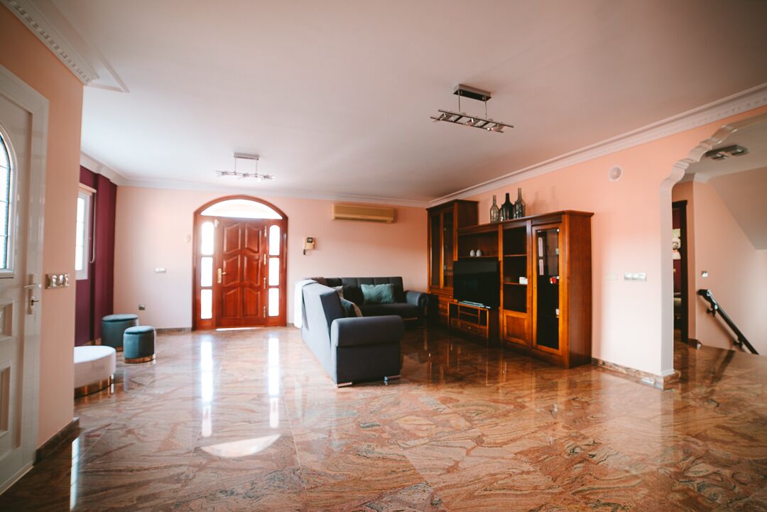 A spacious living room with a marble floor, a sofa, a TV cabinet, and a staircase.