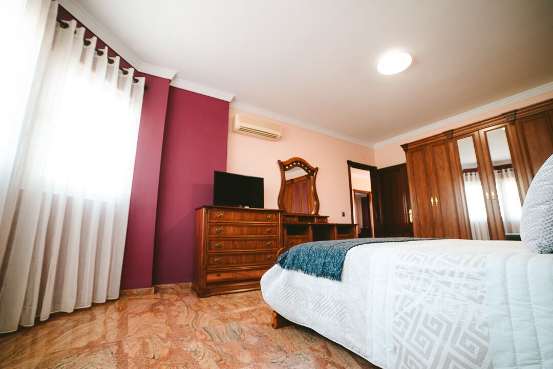 A bedroom with a bed, wooden dresser, and a mirror.