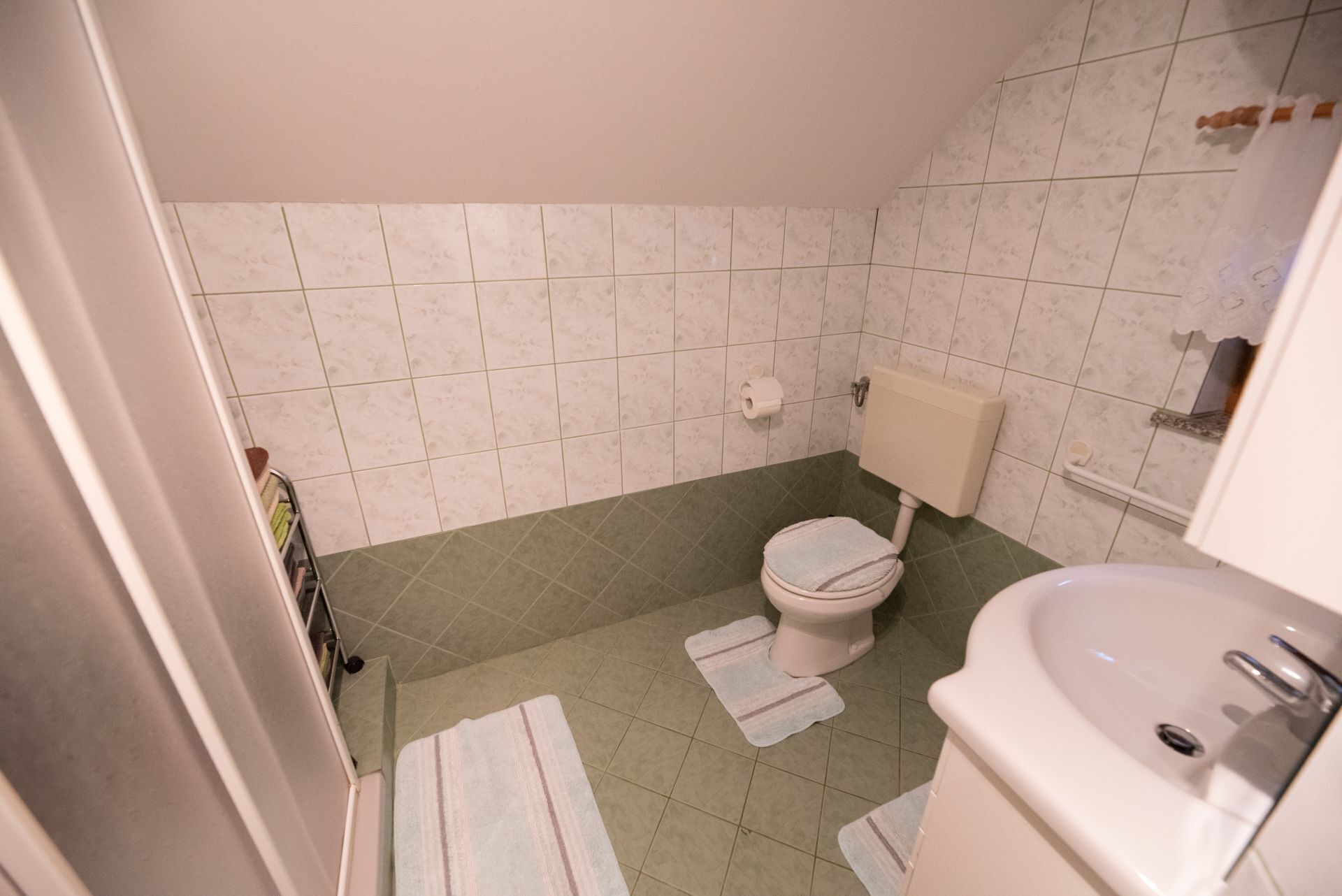 Un baño con inodoro, lavamanos y baldosas de suelo verdes.