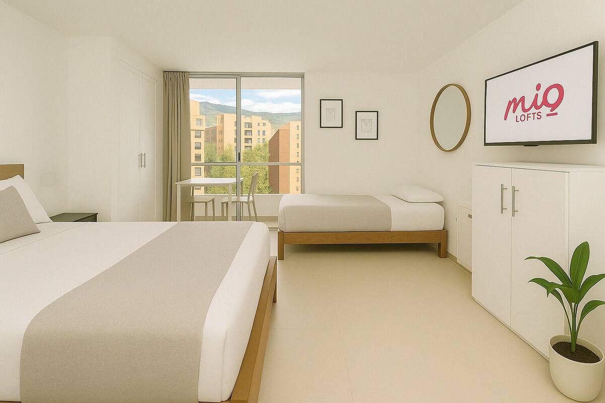 A modern hotel room with a large bed, a smaller bed, a desk, and a wardrobe. There is a window with a view of buildings and a plant on the floor.