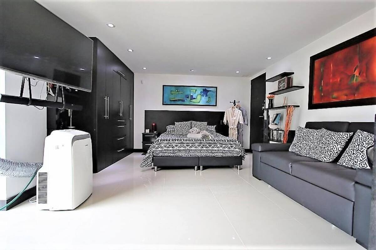 A modern bedroom with a bed, a sofa, a TV, and a large abstract painting.