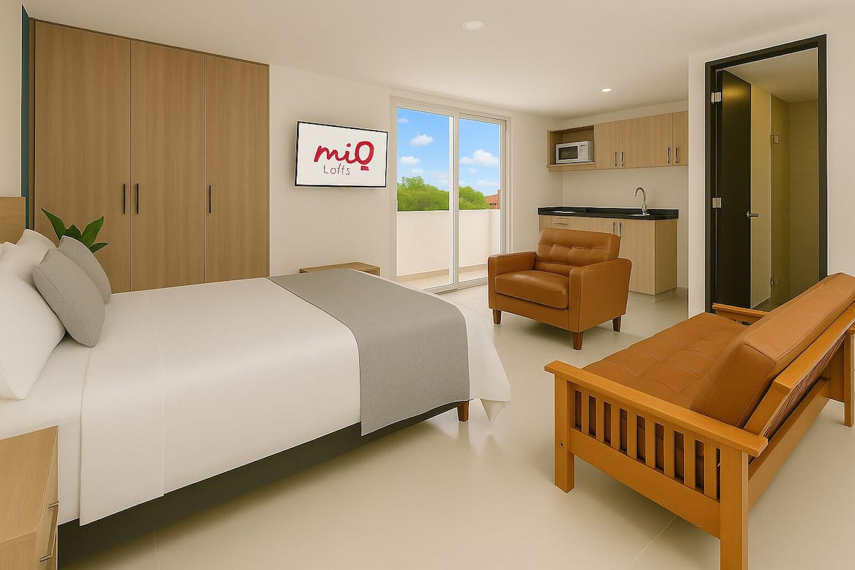 A modern bedroom with a bed, a sofa, and a chair. There is a kitchen area with a microwave and cabinets. A sign with "miQ Lofts" is visible.