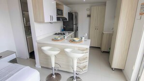 A compact kitchen with a microwave, refrigerator, and two bar stools. - Mio Lofts (Medellín)