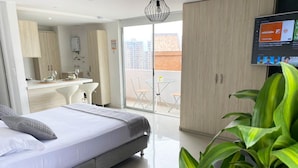A modern hotel room with a bed, a dining area with a table and chairs, a large window, and a TV on the wall. - Mio Lofts (Medellín)