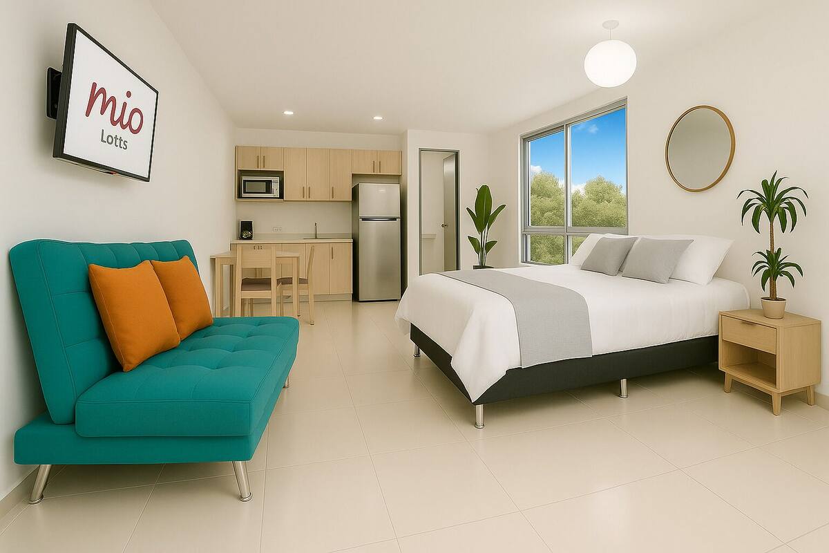A modern bedroom with a bed, a teal sofa, a small kitchen, and a large window.