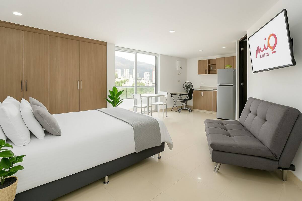 A modern bedroom with a bed, a grey sofa, and a kitchenette.