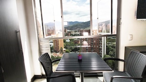 A balcony with a table and two chairs, a potted plant, and a view of a cityscape with buildings and mountains. - Mio Lofts (Medellín)