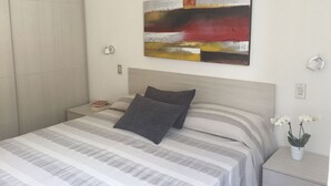 Un dormitorio moderno con cama, mesita de noche, lámpara de pared y un cuadro.