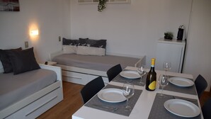 Un espacio habitable compacto con sofá, una mesa de comedor para dos personas y una pequeña zona de kitchenette.