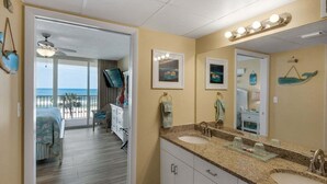 A bathroom with a large mirror, a sink, and a vanity. There is a door leading to a balcony with a view of the ocean.