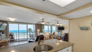 A spacious living area with a kitchen island, large windows, and a balcony with a view of the beach.