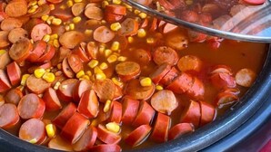 A variety of dishes in a kitchen setting, including a pot with sliced sausage and corn, and another with yellow rice. - Hotel Novo Gama (Novo Gama)