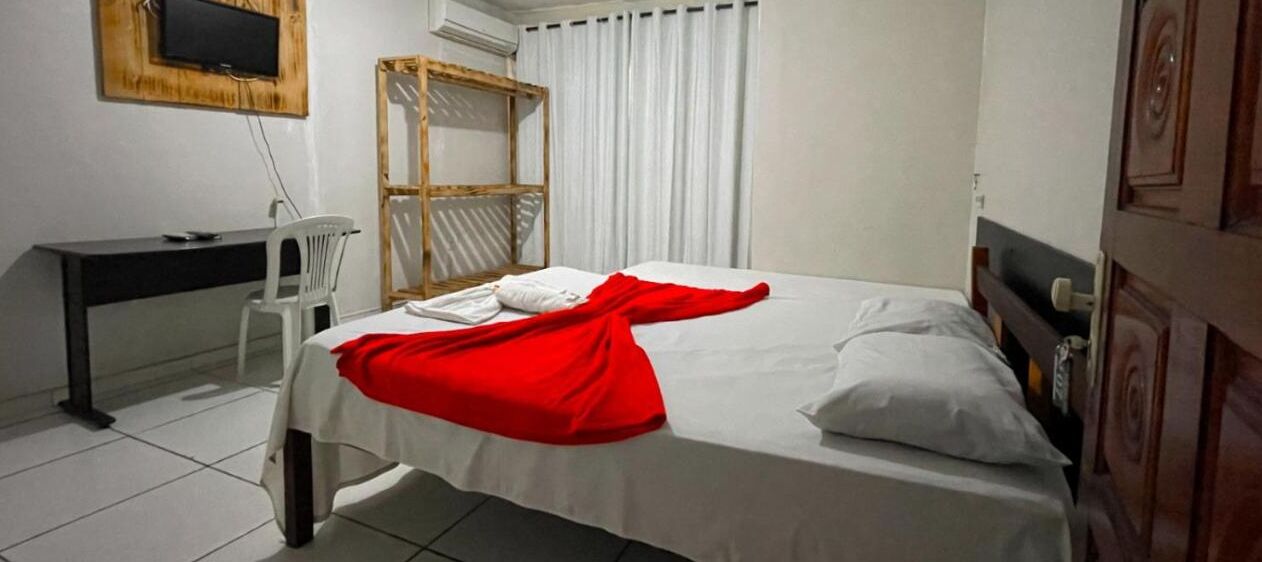 Habitación de hotel con cama, escritorio, silla, televisor y ventana con cortinas.