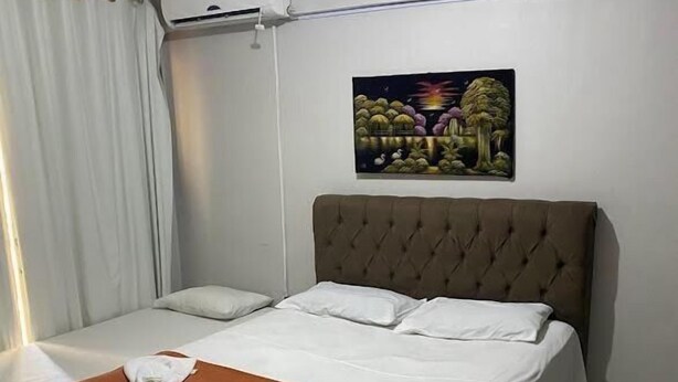 A hotel room with a bed, white curtains, an air conditioning unit, and a painting on the wall. - Hotel Novo Gama (Novo Gama)