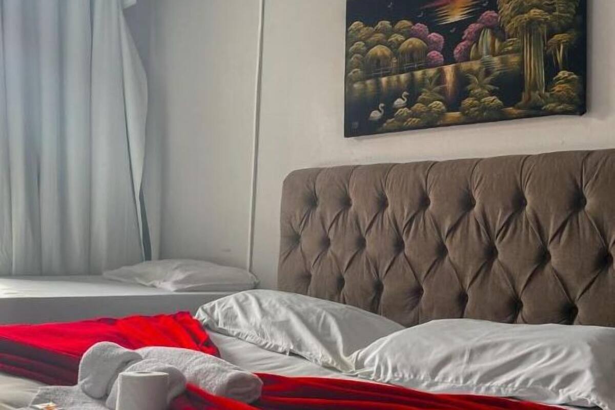 A hotel room with a large bed, a red blanket, and a painting on the wall.