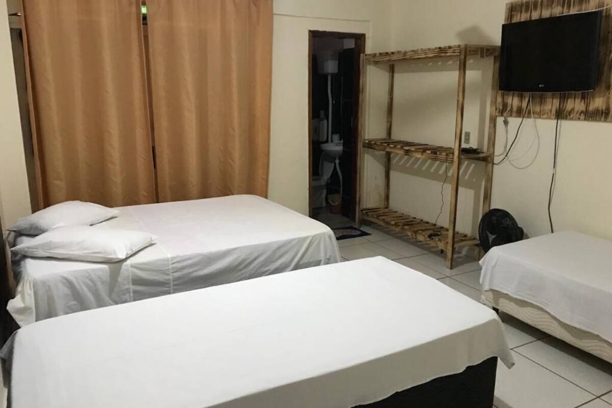 A room with two beds, a TV mounted on the wall, and a wooden shelf unit.