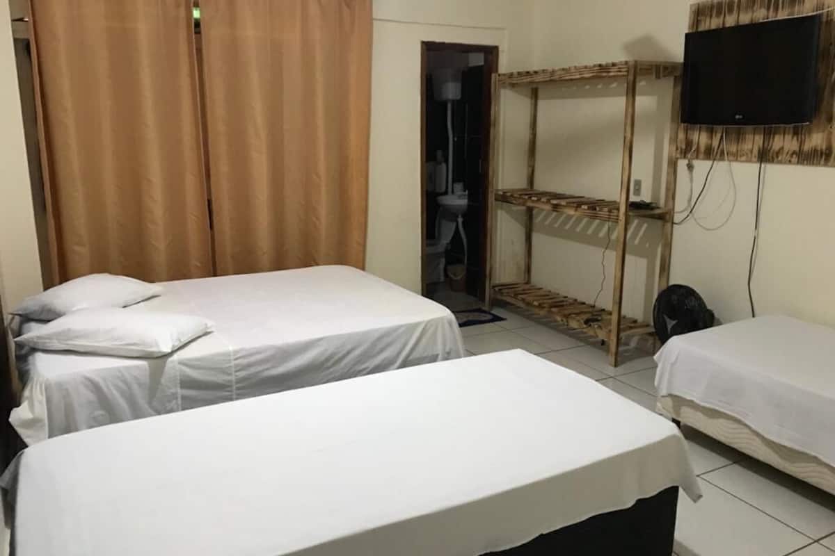 A room with two beds, a TV mounted on the wall, and a wooden shelf unit.