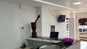 A reception desk with a laptop, a telephone, and a small statue. There is a wall-mounted TV and a door leading outside. - Hotel Novo Gama (Novo Gama)