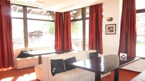 A room with striped sofas, a wooden table, and large windows with red curtains. - Bansko Royal Towers - Apartments (Bansko)