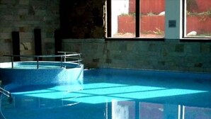 A swimming pool with clear water, surrounded by stone walls and a window with a view of a red fence. - Bansko Royal Towers - Apartments (Bansko)