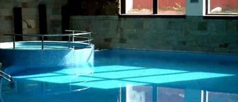 A swimming pool with clear water, surrounded by stone walls and a window with a view of a red fence.