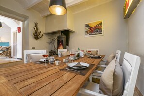Un coin repas avec une table en bois dressée pour quatre personnes, une cheminée et un tableau représentant une voiture de course accroché au mur.