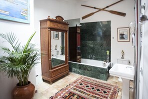 Une salle de bain avec un meuble-lavabo en bois, un grand miroir, une baignoire, un lavabo et un mur en marbre vert.