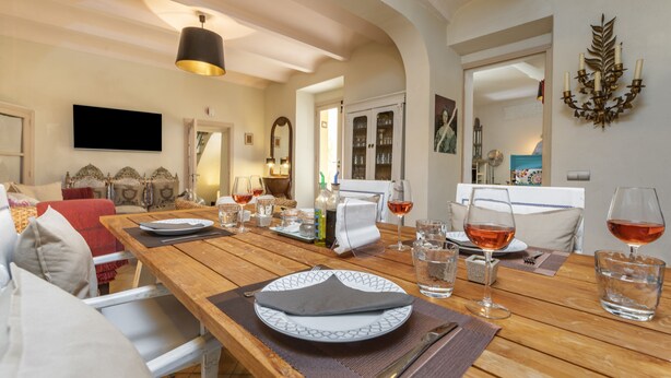 A dining area with a wooden table set for a meal, a television mounted on the wall, and a decorative wall piece.