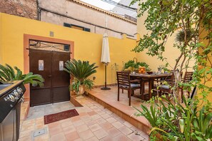 Une terrasse avec une table et des chaises, un barbecue et des plantes en pot.