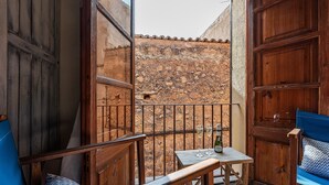 A small balcony with wooden furniture, a table with two glasses, and a stone wall in the background.