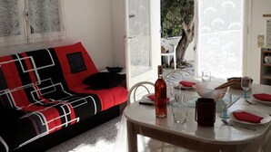 A cozy living area with a red and black sofa, a dining table set with plates, glasses, and a bottle. - NEW: Air-conditioned apartment with wifi (Le Lavandou)