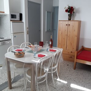 A dining area with a table set for four, chairs, a wooden cabinet, and a kitchenette in the background. - NEW: Air-conditioned apartment with wifi (Le Lavandou)