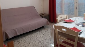 A room with a bed, a dining table set for two, a red curtain, and a view through a glass door.