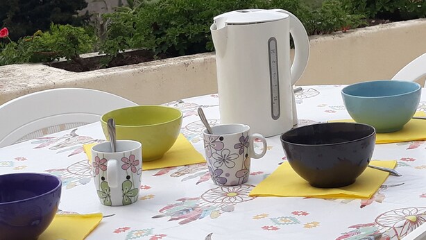 A table with various bowls and a kettle, set against a scenic view of hills and a body of water.