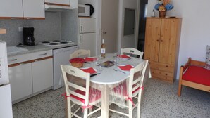 A compact kitchen with white cabinets, a microwave, a coffee maker, and a dining table set for two with chairs.