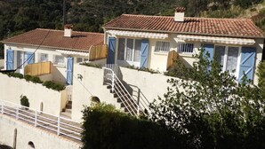 A coastal building with a tiled roof, blue shutters, and a staircase leading to the upper floor.