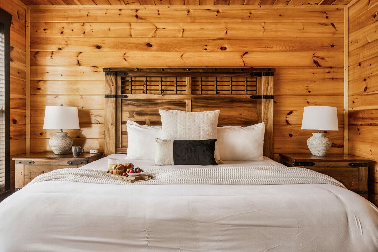 A wooden cabin bedroom with a bed, pillows, bedside tables, and a tray of snacks.