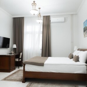 A hotel room with a bed, a desk with a lamp, a TV, and an air conditioning unit. - Jardin Hotel Belgrade (Belgrade)