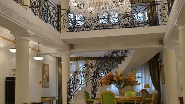 A grand lobby with a staircase, a chandelier, and a dining area with green chairs and a vase of flowers. - Jardin Hotel Belgrade (Belgrade)
