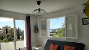 Ett rum med en soffa, ett bord med vinglas, en vinflaska och utsikt över havet genom stora fönster.