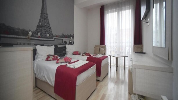 A hotel room with two beds, a TV, a small table, and a view of the Eiffel Tower on the wall. - MM Rooms (Skopje)