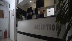 A reception area with a white reception desk, a fire extinguisher, and a plant. - MM Rooms (Skopje)