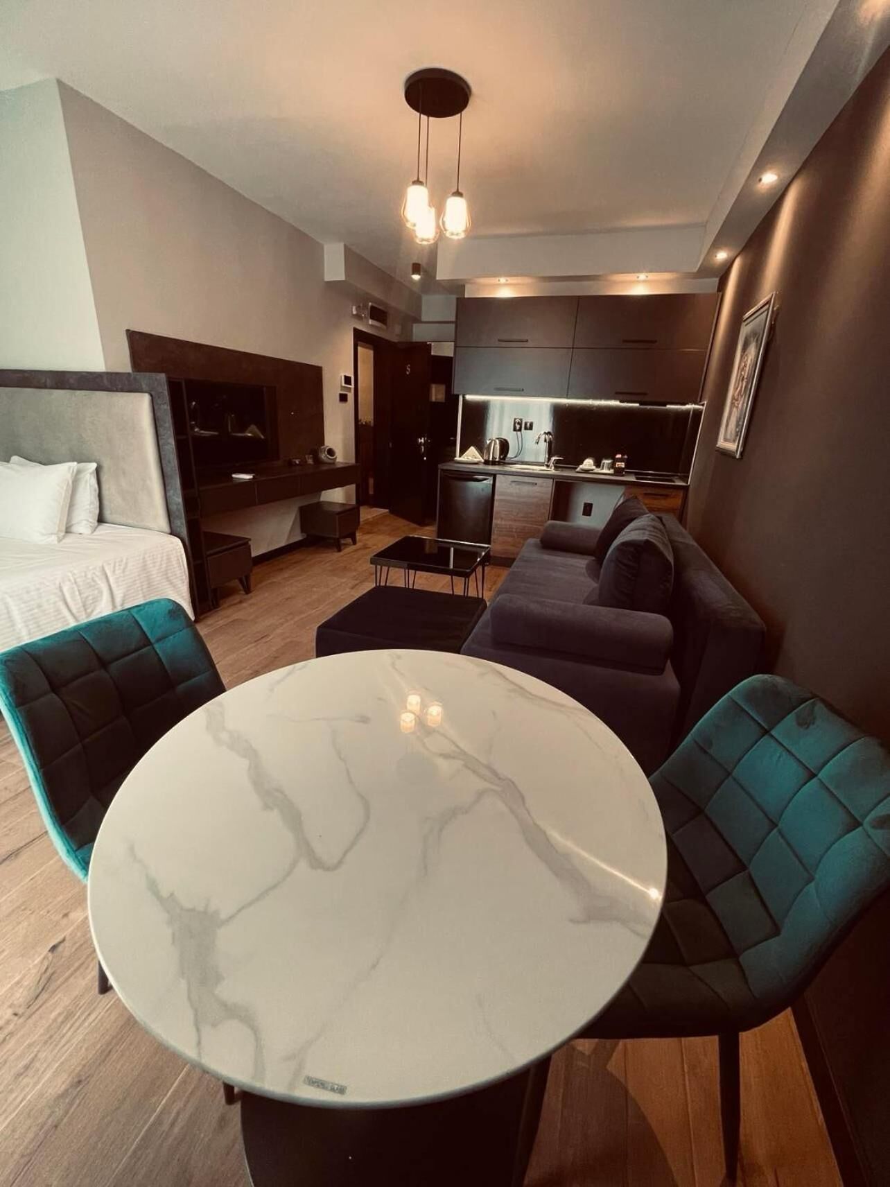 Ein modernes Hotelzimmer mit Bett, einer Couch, einem Esstisch und einer Küchenzeile.