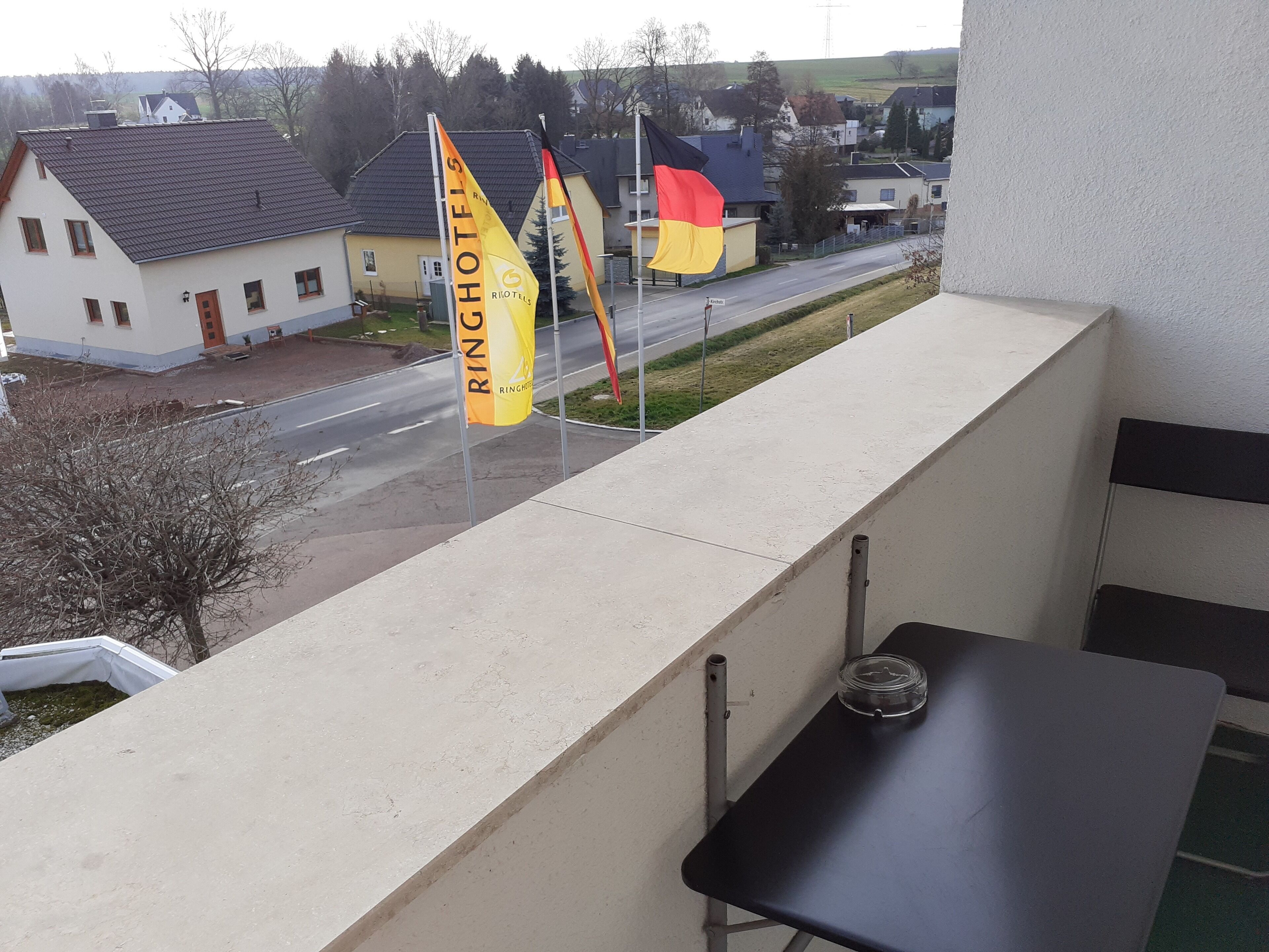 A balcony with a view of a street, a flag, and a table.