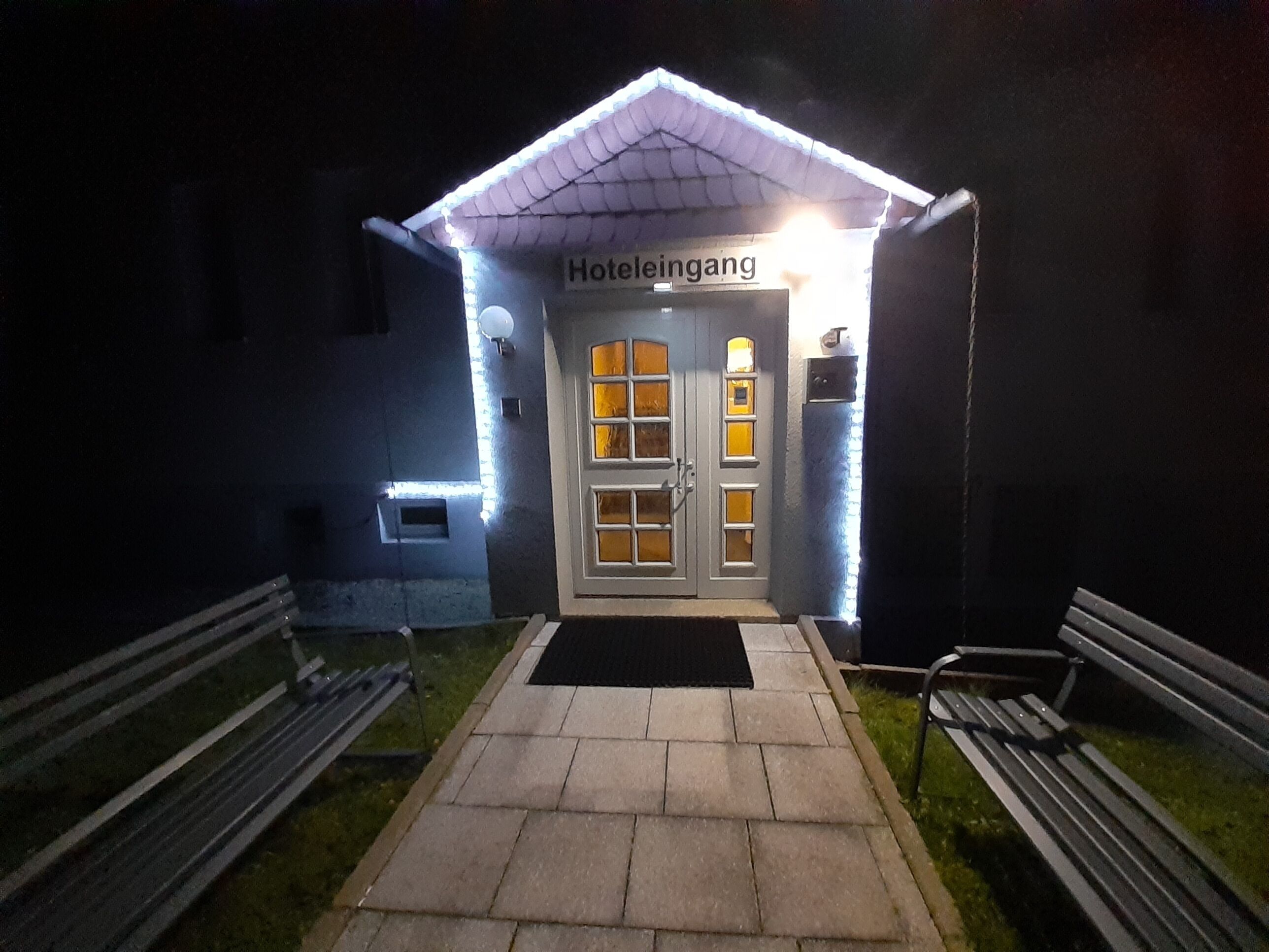 Entrada de hotel con un cartel que dice 'Hotelleingang' y un sendero de baldosas que conduce a la puerta.
