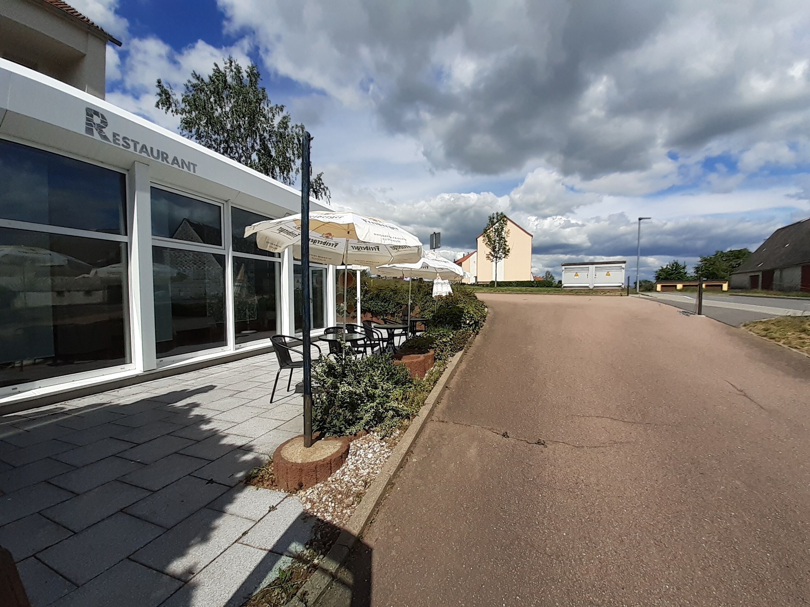 A restaurant with outdoor seating, a paved sidewalk, and a clear sky.