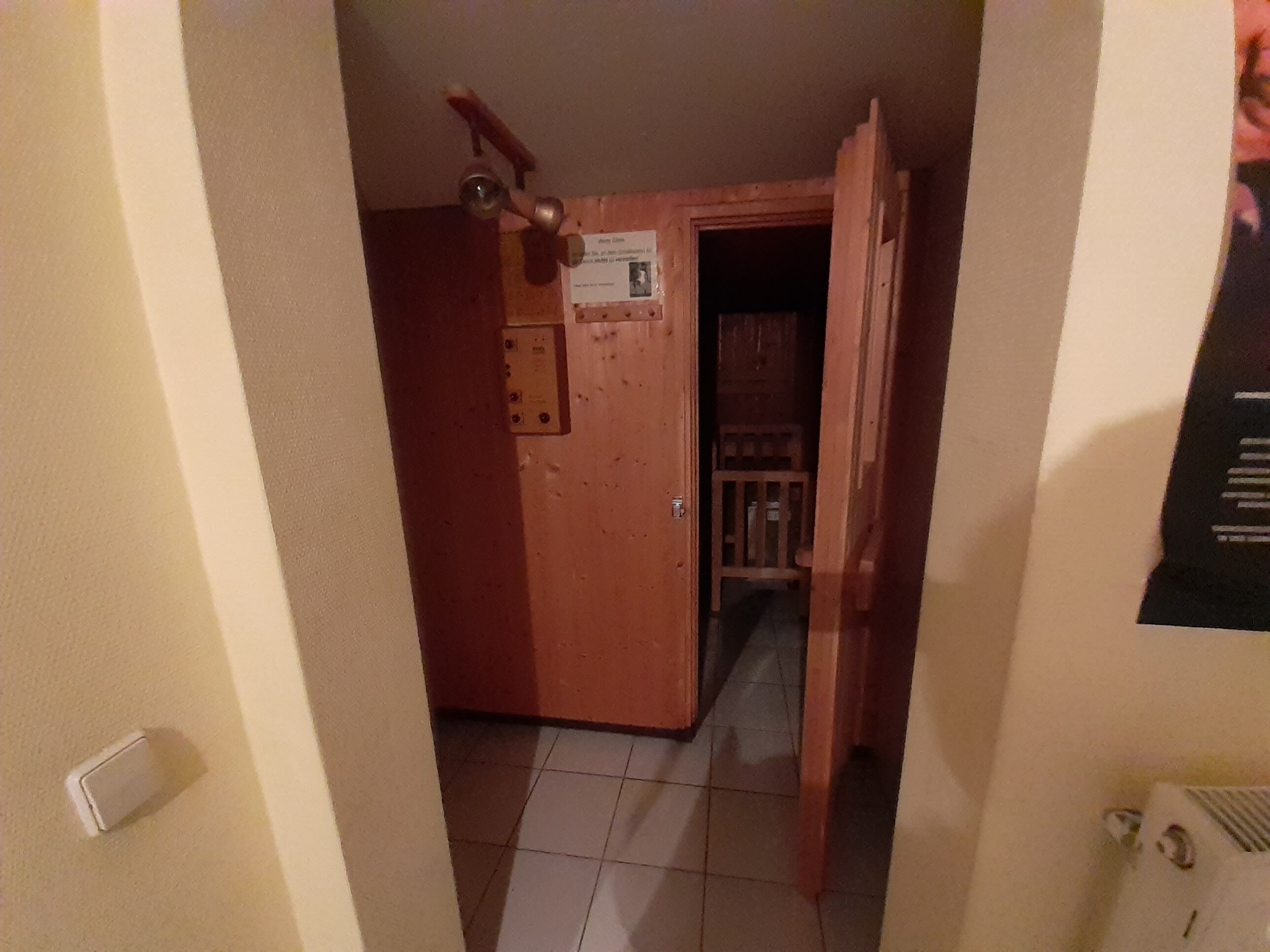 Ein schmaler Korridor mit einer Holztür, einem kleinen Schild und einem Heizkörper an der Wand.