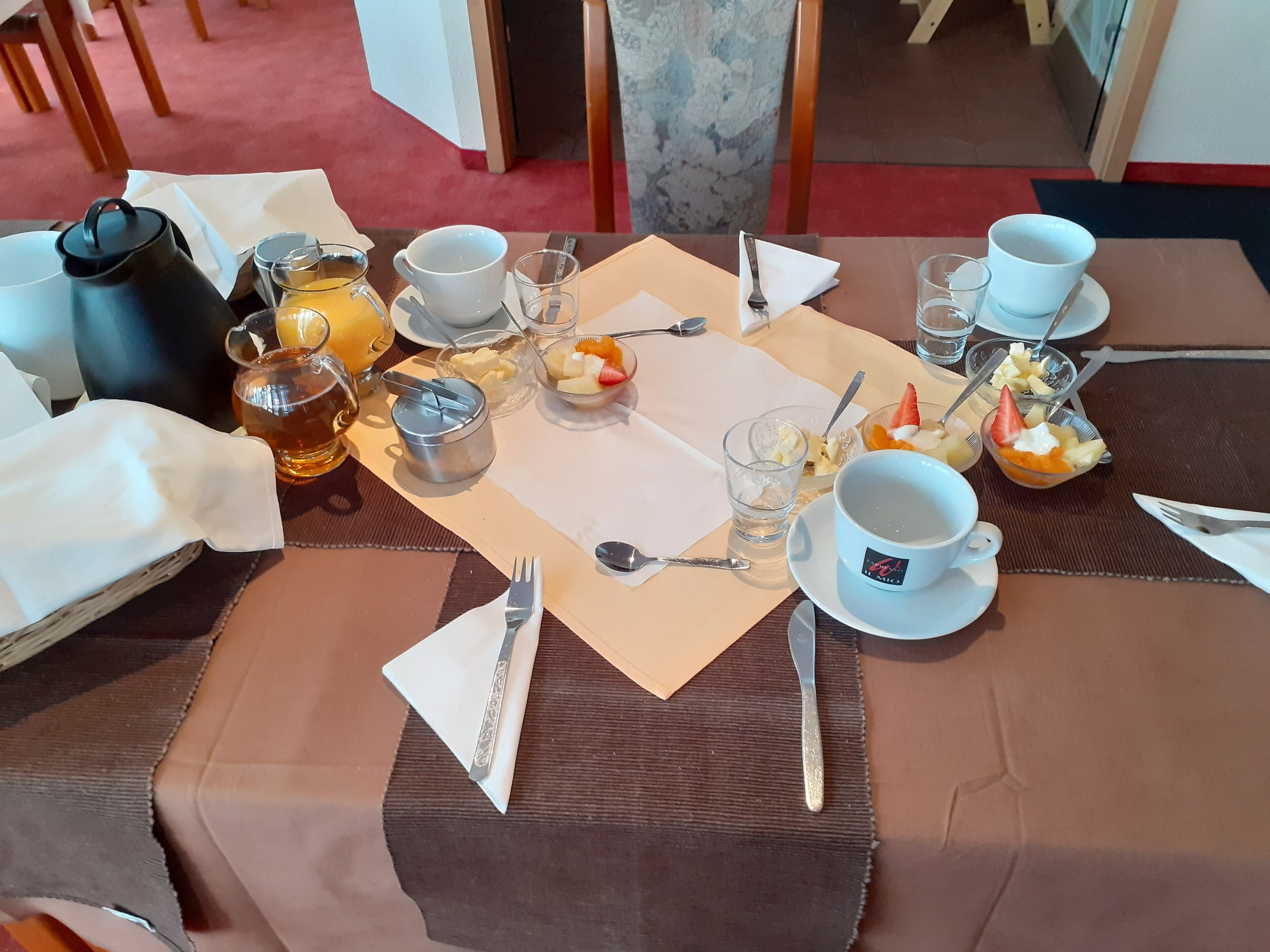 A breakfast table set with various dishes, including fruit bowls, a teapot, and cups.
